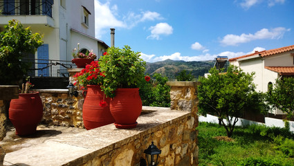 Naklejka premium The decoration on Greek street - large bright clay flower pots and geraniums in it.