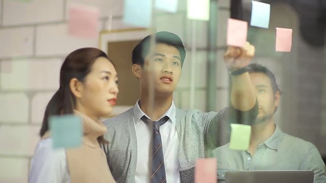 group of asian entrepreneur discussing business in office using adhesive notes