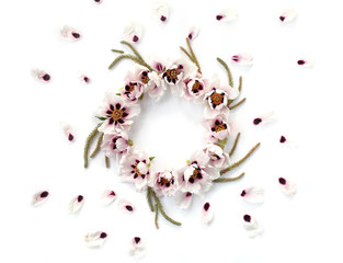 Round floral frame made of white peonies, big evergreen branches and falling petals on white background. Top view, flat lay.