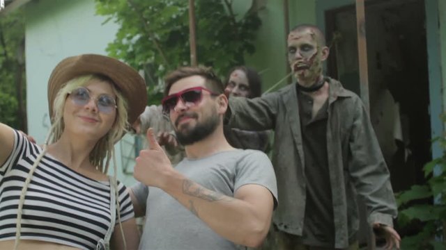A young couple takes a selfie on the background of linked zombies.