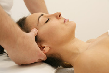 Fototapeta na wymiar Esthetician massaging head and face of young woman during Facial