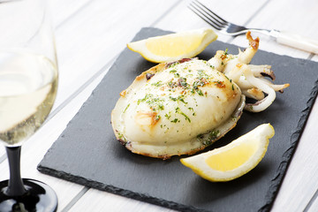 Cuttlefish with garlic and parsley, lemon next to white wine glass on whiteboard. Food.