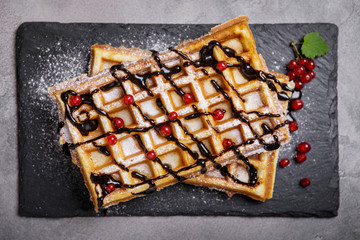 Plate of belgian waffles with chocolate sauce and currant fruit on dark gray background
