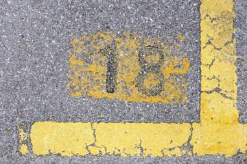 Yellow imprint of the number eighteen on a tarmac pavement.
