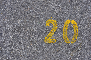 Yellow imprint of the number twenty on an asphalt road.