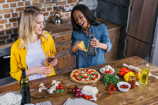 Smiling Young Multiethnic Women Preparing Pizza And Drinking Wine In Kitchen