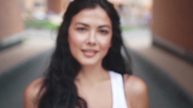 young woman walks through city, she stops in front of camera and smiles. young woman in jeans and a t-shirt walking in the summer city. slow motion