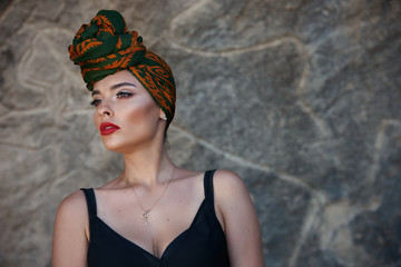 Beautiful fashion east woman portrait with oriental accessories and colorfull shawl on head on the background of rock paintings.