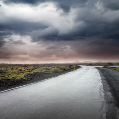 Empty rural road under dark dramatic stormy sky