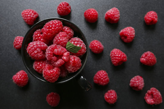 closeup of fresh raspberries in a cup on black background