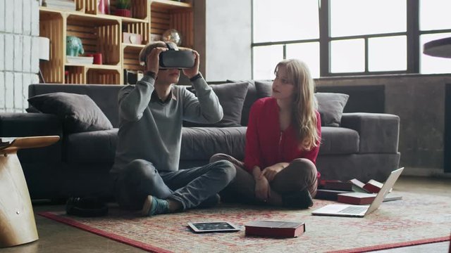 Couple of young woman and man using virtual reality glasses at home in living room