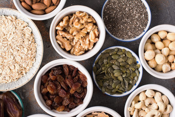 Ingredients for homemade paleo granola, different nuts and raisins, dates, seed on the grey stone background, top view