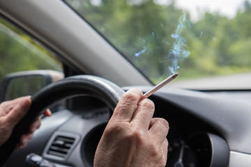 Smoking cigarette in the hand of elderly woman at steering wheel