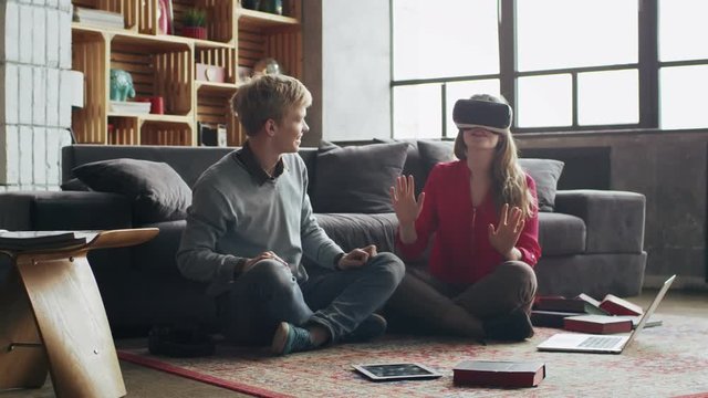 Couple of young woman and man using virtual reality glasses at home in living room