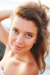 Sunny large portrait of a girl with flying hair at sunset, she smiles