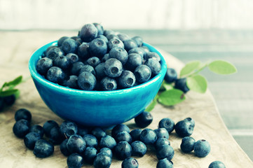 Berries of ripe juicy bilberry in a blue small bowl on a wooden table. Harvest of wild berries
