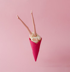 Doll legs in vanilla ice cream with red cone on pink pastel background. Creative summer concept.