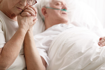 Senior man in hospital bed and his wife holding his hand - obrazy, fototapety, plakaty