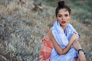 Fashion portrait of beautiful sexy female brunette girl model sitting  in green summer bright grass in the park with make-up in oriental scarf.perfect skin.nature