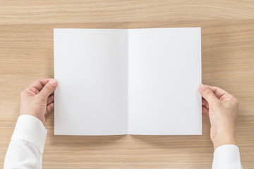 Obraz premium Mock up flyer pamphlet brochure design A5 size paper in business man's hand for template illustration mockup, flat lay on wood table from top view