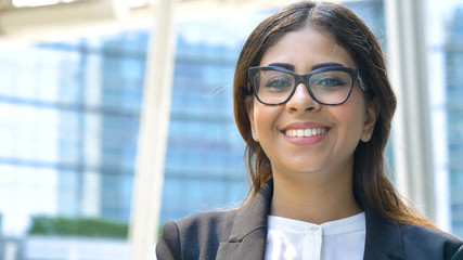 Portrait of young beautiful business woman (student) in suit, glasses, smiling, happy, walking down stairs, steps, on building background. Concept: new business, communication, Arab, banker, manager.