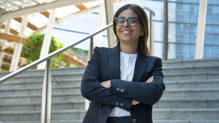 Fototapeta premium Portrait of young beautiful business woman (student) in suit, glasses, smiling, happy, walking down stairs, steps, on building background. Concept: new business, communication, Arab, banker, manager.