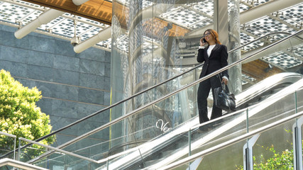 Young beautiful business woman (student) in a suit, glasses, smiling, happy, holding a phone, bag, walking down the escalator, steps, successful. Concept: new business, communication, Arab, banker.