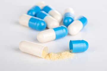 Open blue capsule with yellow powder drug on the white background.