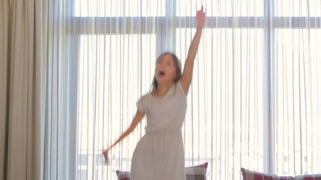 The girl is jumping on the couch. The girl is dancing on the couch. The child is having fun. The girl is happy and laughs. A happy girl.