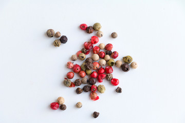 Different types of peppercorns - black, white, pink and green pepe verde - on white. Top view. Copy...
