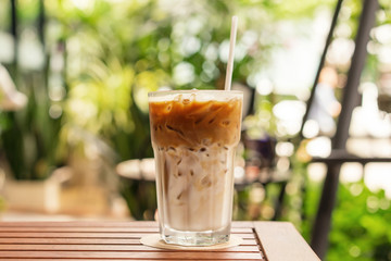 Glass of Ice latte on wooden table at cafeteria, front close up