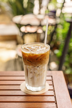 Glass of Ice coffee with milk on a wooden table at cafeteria, close up