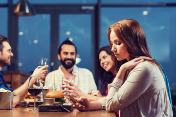 woman with smartphone and friends at restaurant