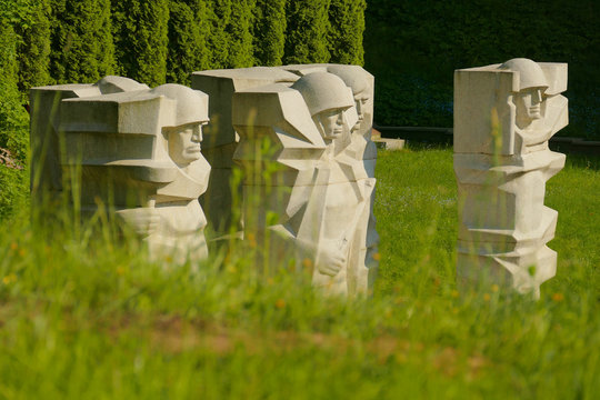 Monument depicting the silhouettes of Soviet soldiers at the Vilnius cemetery. Behind green grass there are blocks of stone from which carved soldiers in helmets.