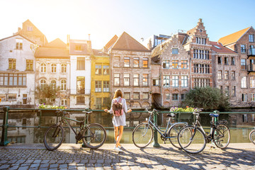 Sunrise view on the water channel with beautiful old buildings with woman standing near the bicycles in Gent city - obrazy, fototapety, plakaty