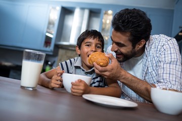 Man feeding croissant to son