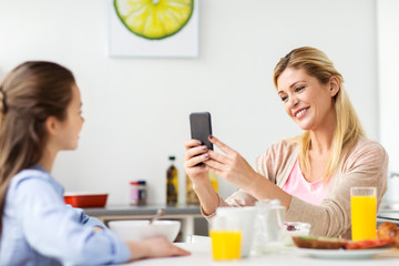 woman photographing daughter by smartphone at home