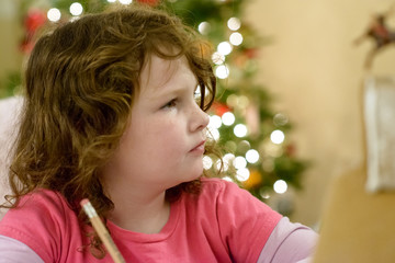 Fototapeta premium Cute little child girl writes the letter to Santa Claus near Christmas tree indoors.