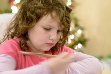 Fototapeta premium Cute little child girl writes the letter to Santa Claus near Christmas tree indoors.
