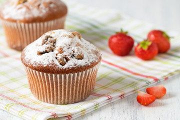 Freshly baked muffins with strawberries, dusted with powdered sugar on a white wooden background.