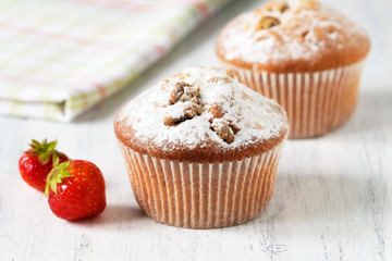 Freshly baked muffins with strawberries, dusted with powdered sugar on a white wooden background.
