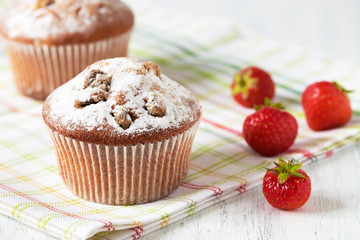 Freshly baked muffins with strawberries, dusted with powdered sugar on a white wooden background.
