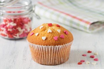 Freshly baked muffins with candy sprinkles hearts on white wooden background.