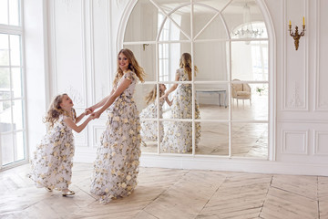 mother and daughter dancing in the mirror in the same dress in a big white room
