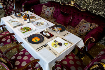 A table served by dishes for six people. Seasoned table with salad, mushroom cream soup, baked fish, wine and cognac