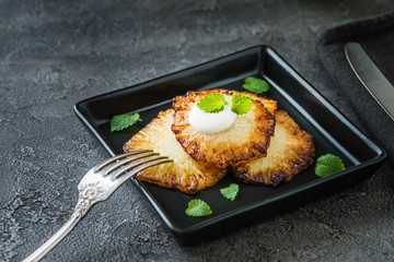 Fried pineapple slices with creme fraiche, dark background