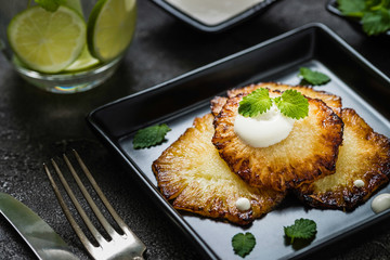 Fried pineapple slices with creme fraiche, dark background