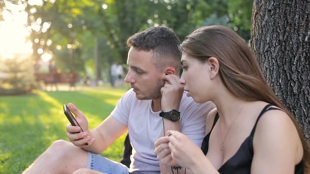Guy and girl listening to music on the phone in a park under a tree