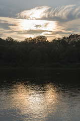 Fototapeta premium River running across with reflections in the water. Evening sunset with pink and violets colors in the sky. Silhouettes