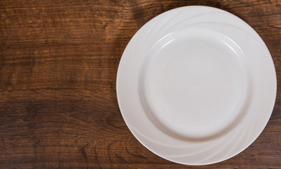 Empty white plate on the brown wooden table background. with copy space. top view.
